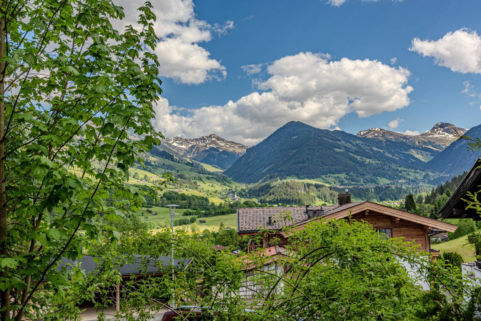 Panoramablick auf die umliegende Berglandschaft mit grünen Tälern und traditionellen Häusern unter blauem Himmel.