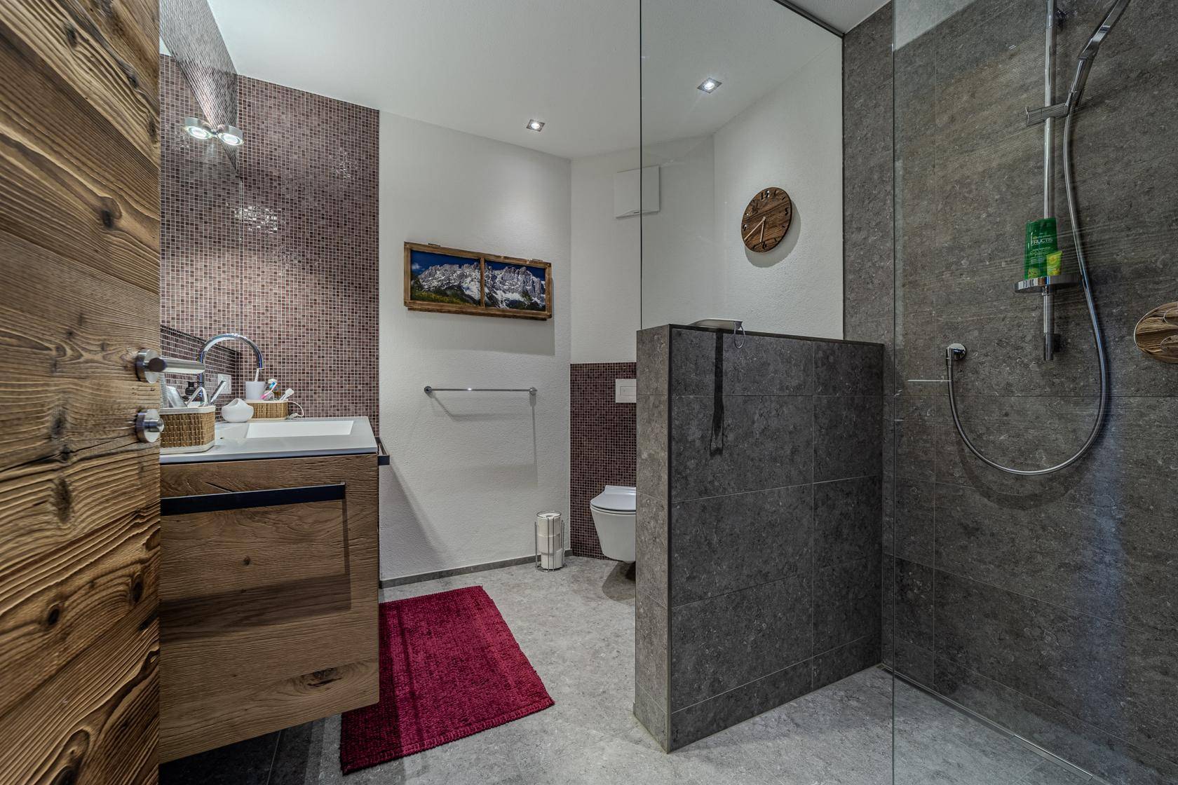 Modernes Badezimmer mit begehbarer Dusche, Holzelementen und dunklen Fliesen.