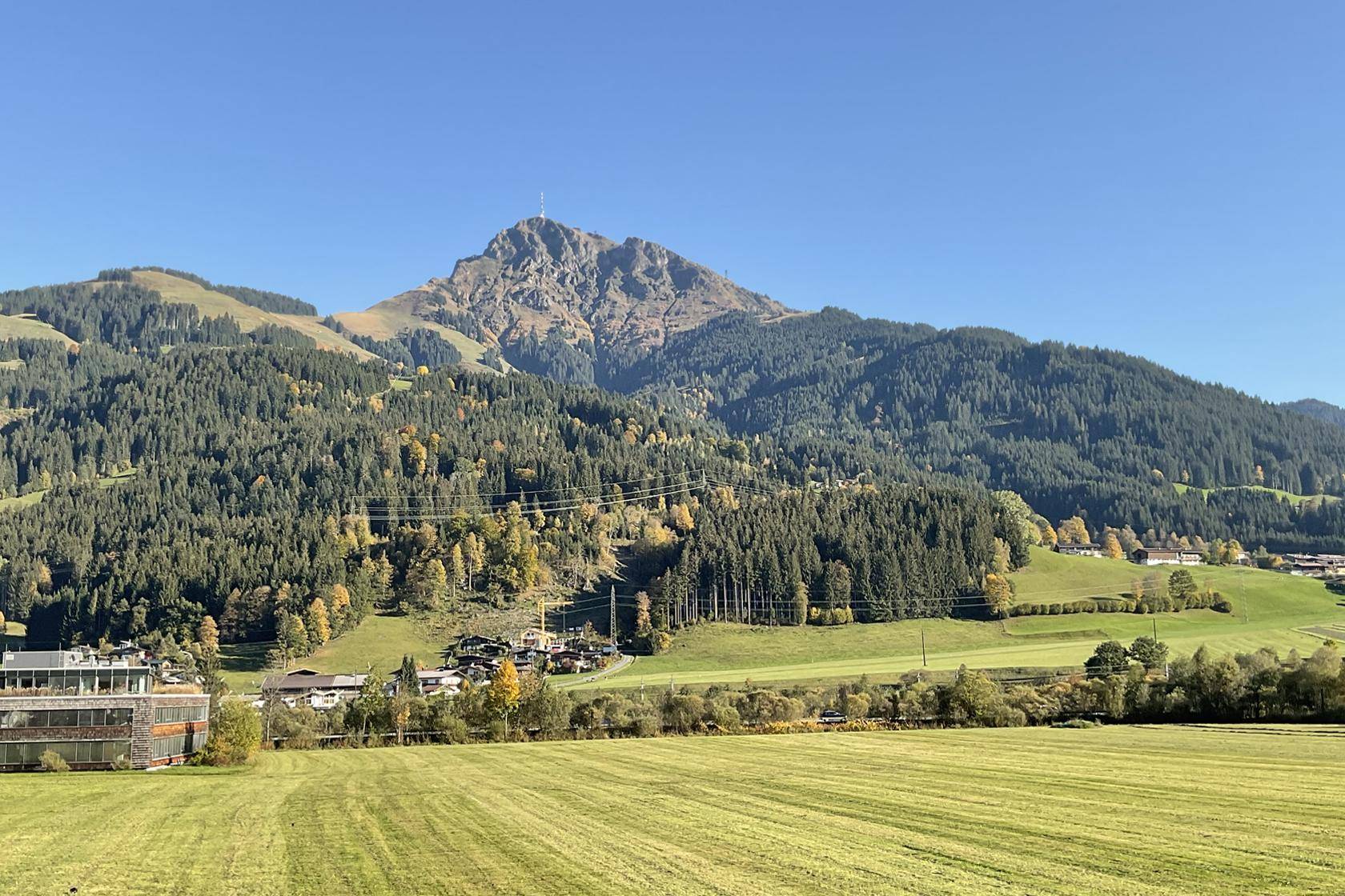 Malerische Berglandschaft mit grünen Wäldern und Wiesen unter strahlend blauem Himmel.