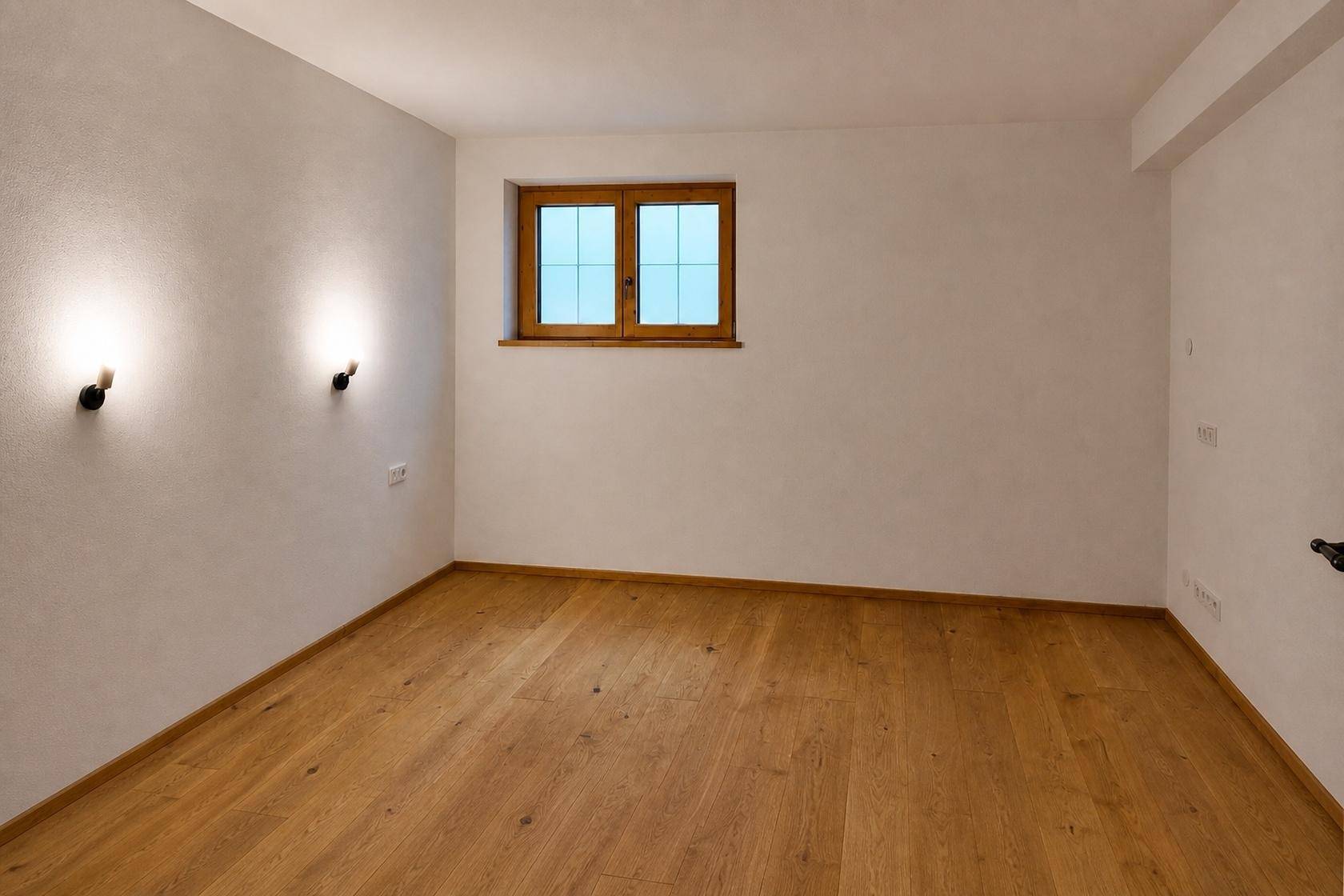 Leeres Schlafzimmer mit Holzboden und einem Fenster, das für natürliche Belichtung sorgt und eine ruhige Atmosphäre schafft.