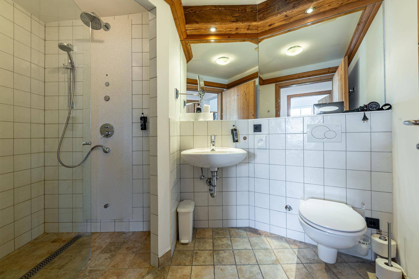Helles Badezimmer mit großer begehbarer Dusche, WC und Waschbecken, unter Holzbalken.
