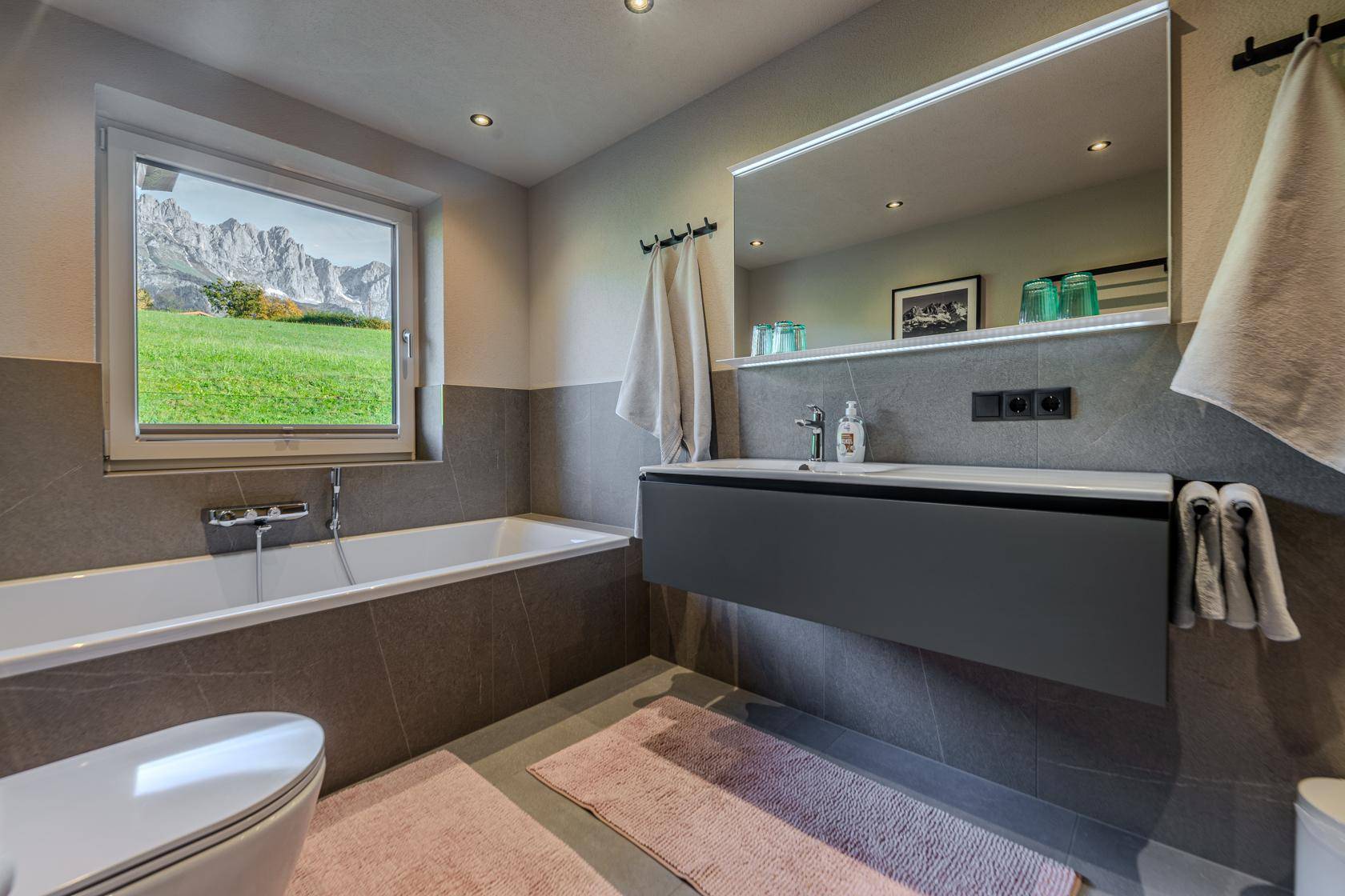 Modernes Badezimmer mit Badewanne, schwebendem Waschtisch und Fenster mit Bergblick.