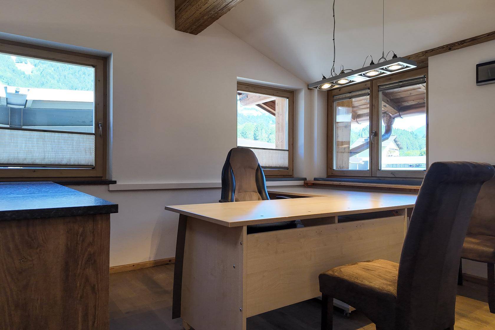 Helles Büro mit Holztisch, Bürostuhl und Fenstern, die einen Blick auf die umliegende Landschaft bieten.