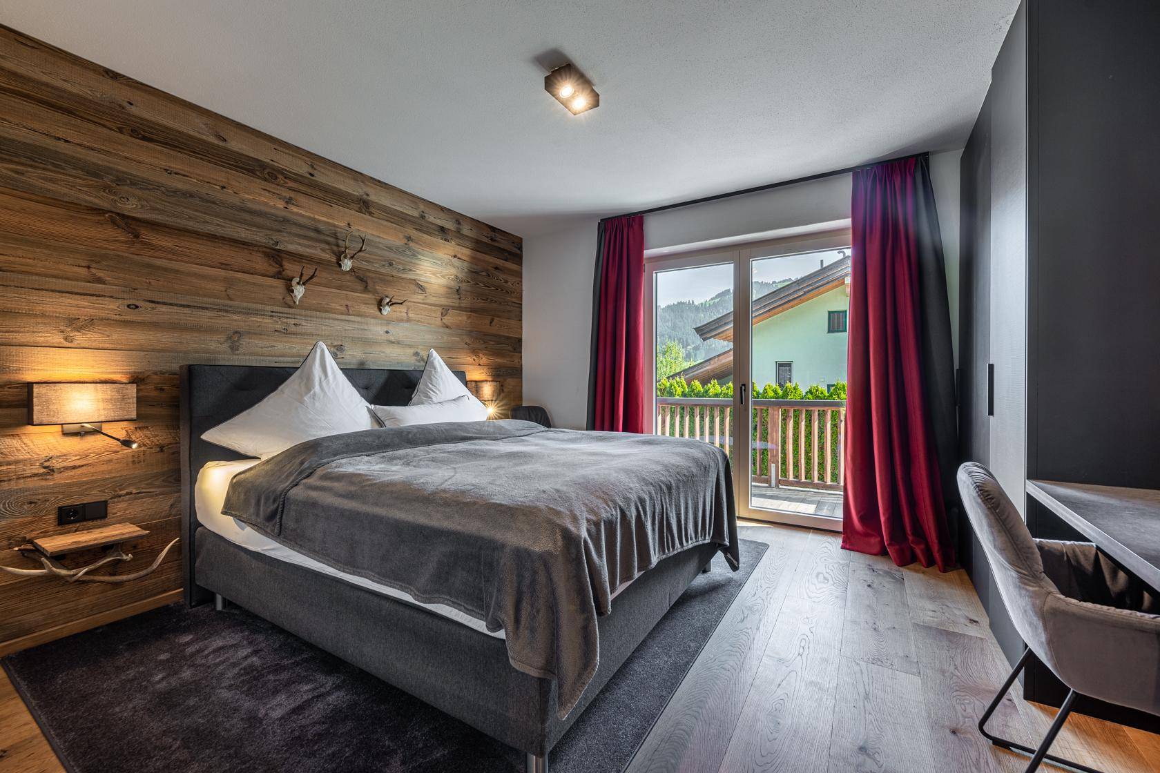 Gemütliches Schlafzimmer mit Holzwand, Doppelbett und Zugang zu einem Balkon.