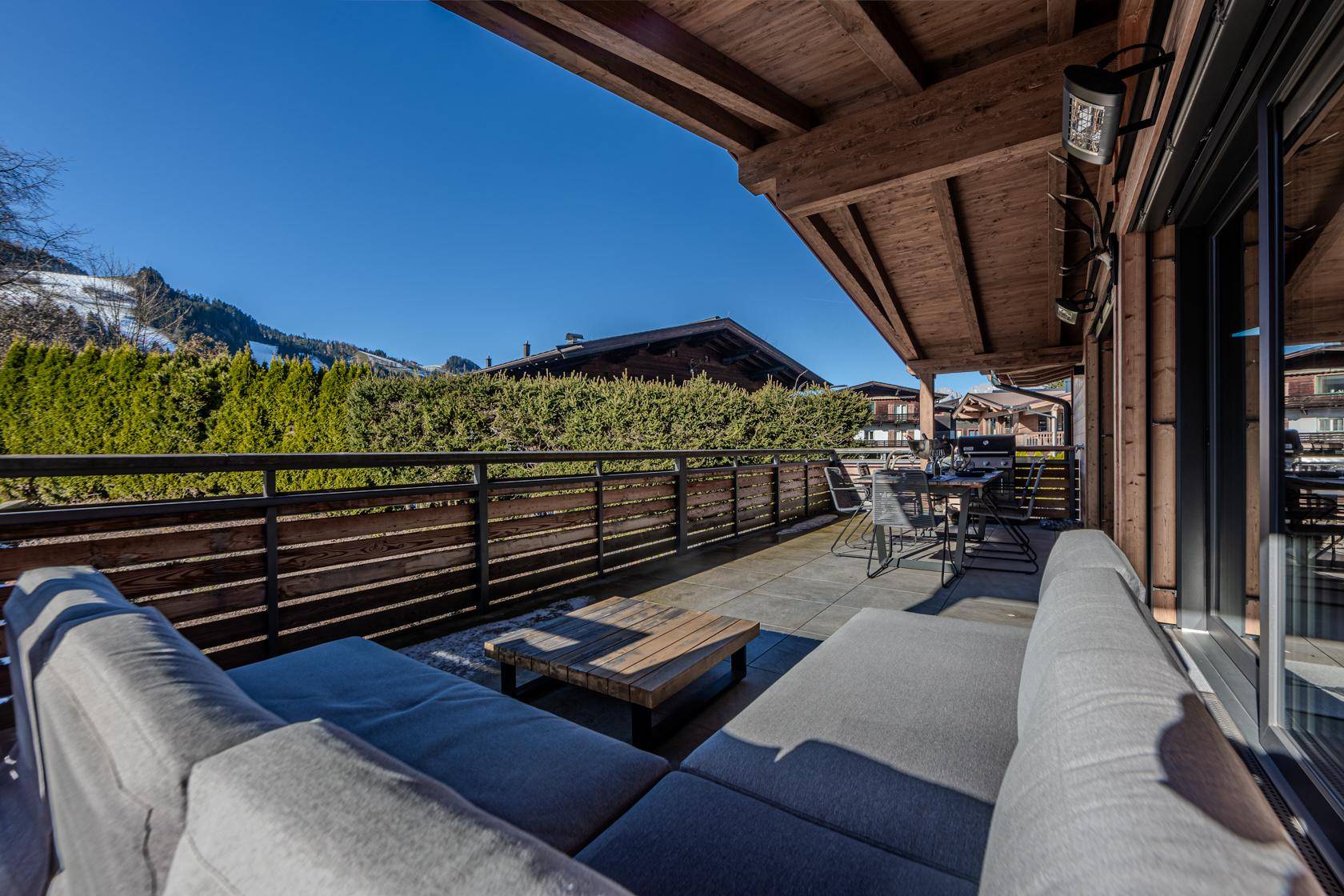 Weitläufige Terrasse mit bequemen Lounge-Möbeln und Blick auf die umliegende Berglandschaft und Hecken.