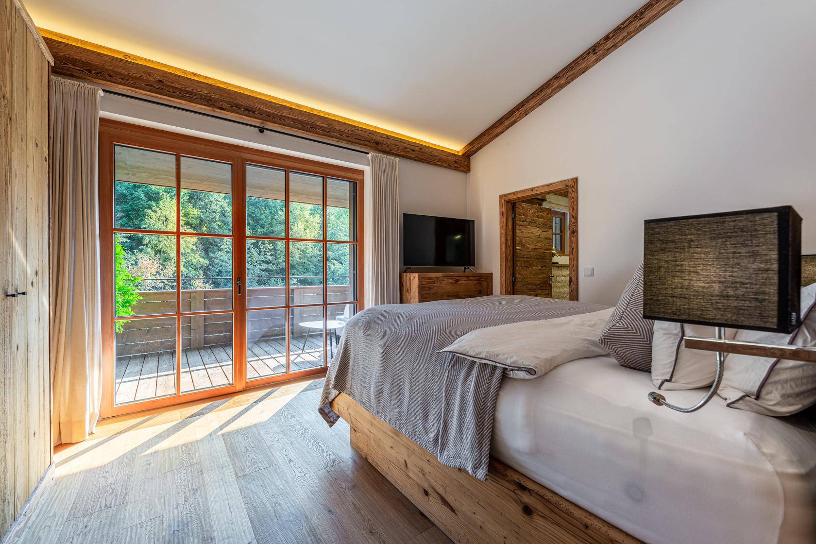 Helles Schlafzimmer mit Holzboden, Balkonzugang und Blick auf die grüne Umgebung.