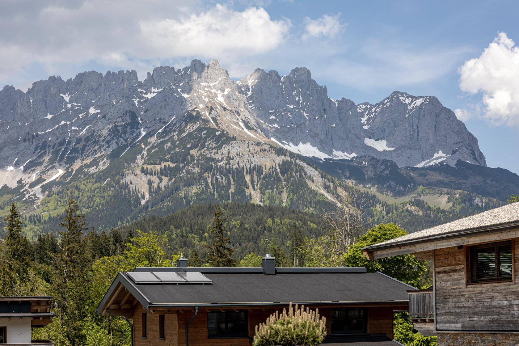 Beeindruckende Bergkette über einem Hausdach mit Photovoltaikanlage in sonniger Umgebung.