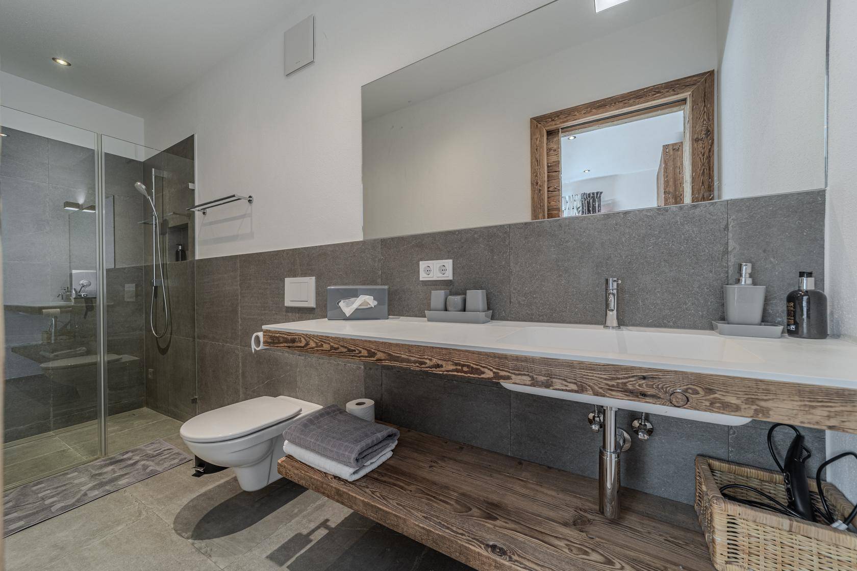 Modernes Badezimmer mit großem Spiegel, Dusche und Holzwaschtisch.