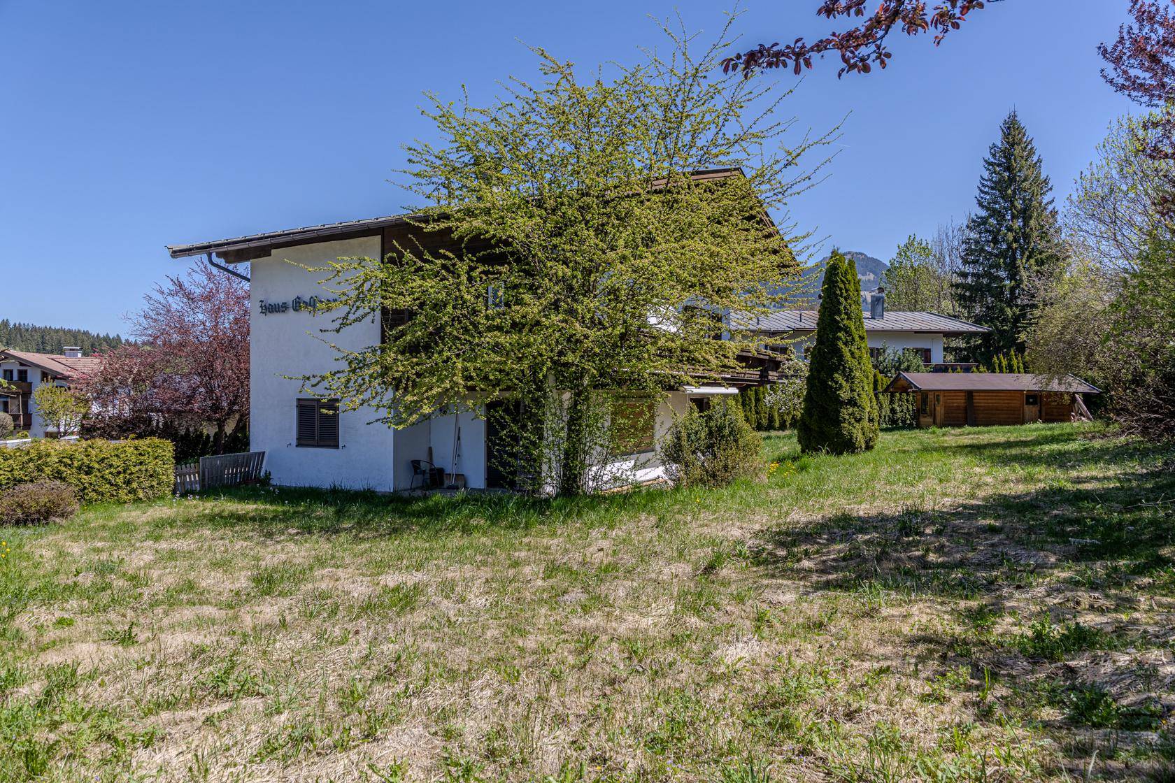 Außenansicht eines Hauses mit weißer Fassade, braunem Dach und großem Garten.