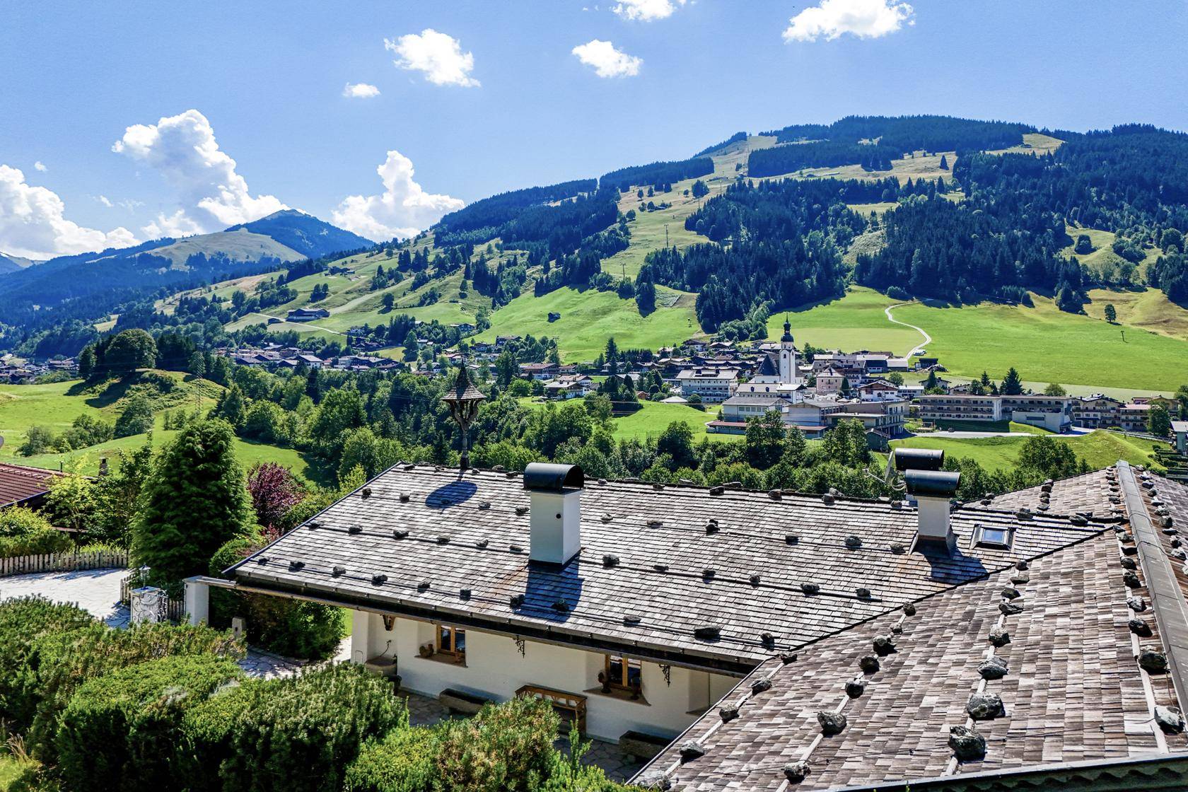 Panoramablick über ein malerisches Alpendorf und die umliegende Berglandschaft unter blauem Himmel.