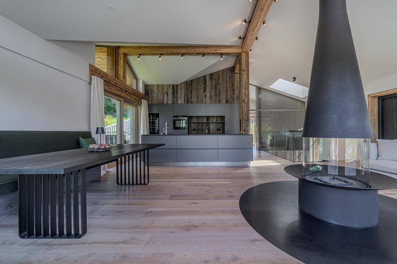 Offener Wohnbereich mit moderner Küche, Esstisch und freistehendem Kamin in Holzarchitektur.
