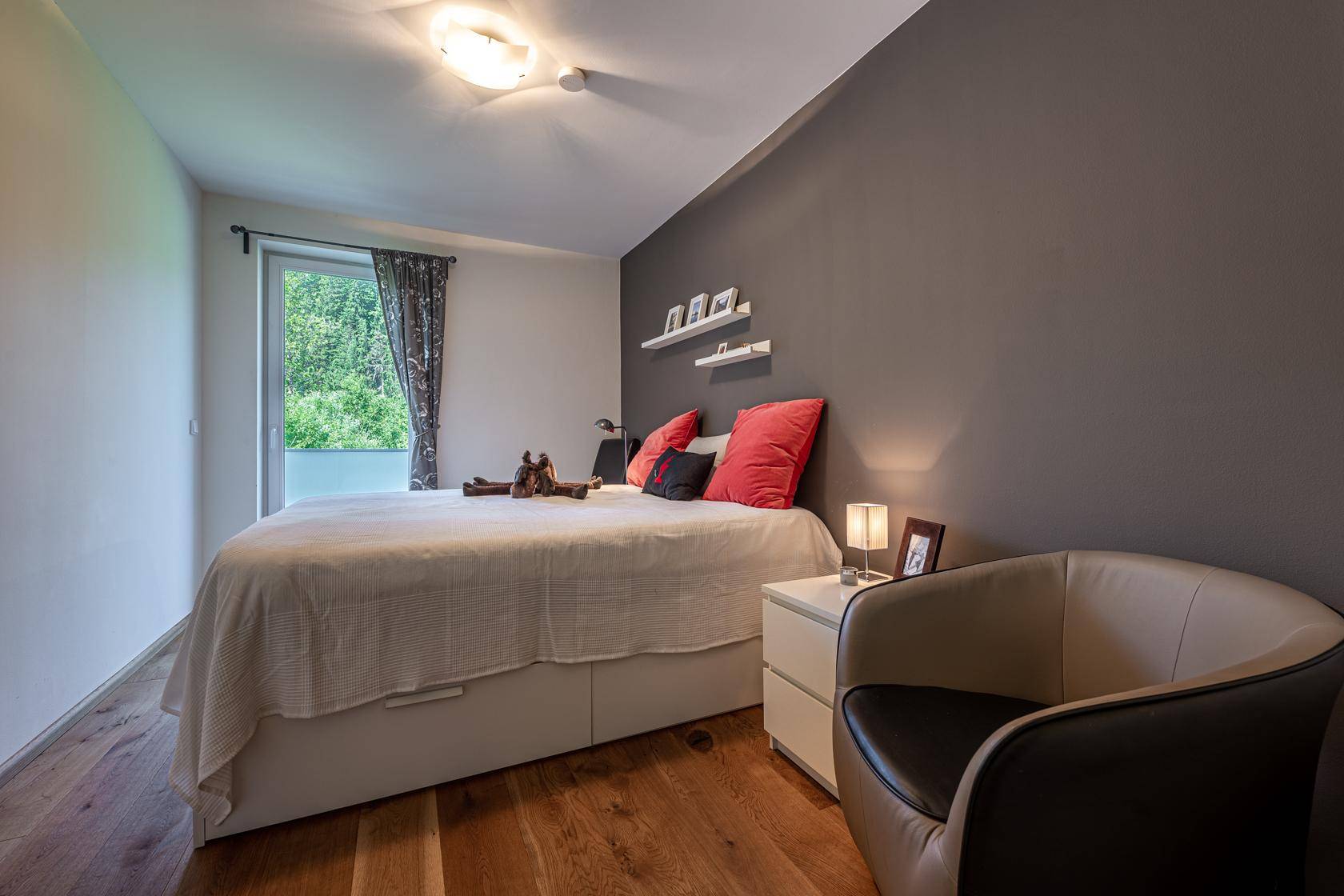 Gemütliches Schlafzimmer mit Holzboden, dunkler Akzentwand und Balkonzugang.