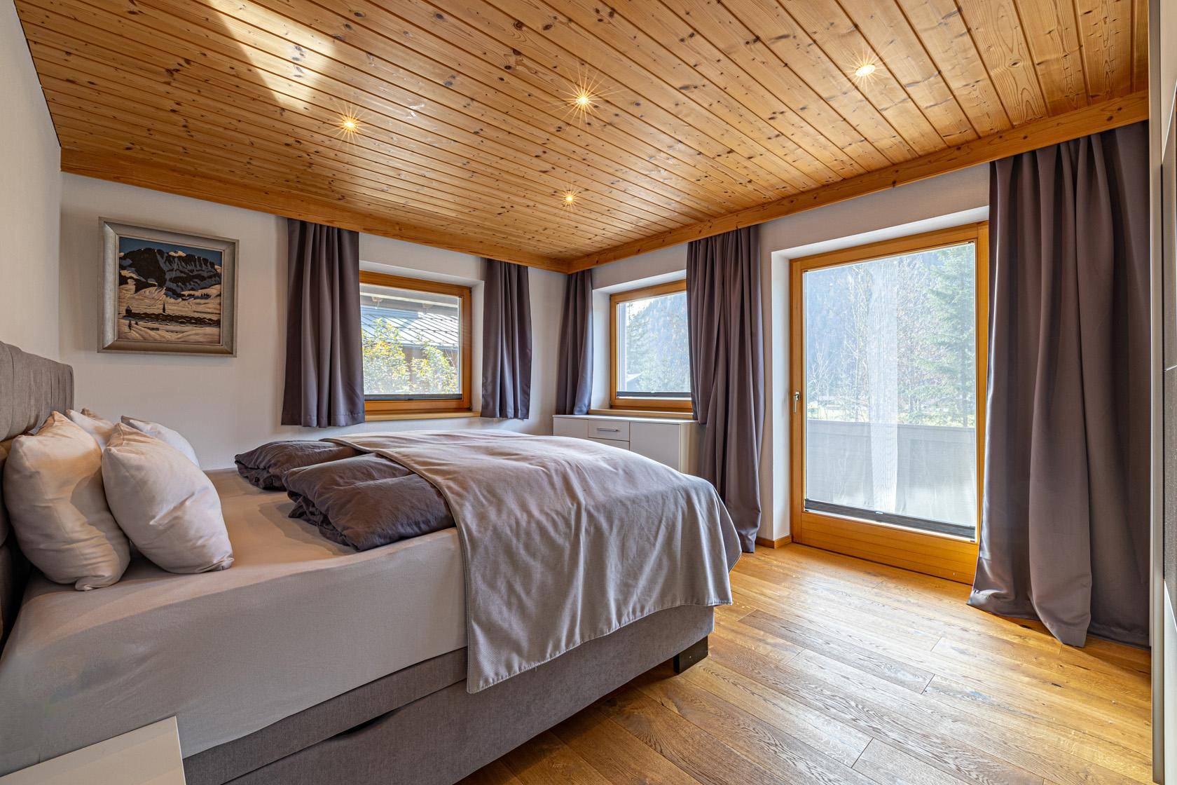 Gemütliches Schlafzimmer mit Holzboden, Holzdecke und Zugang zum Balkon.