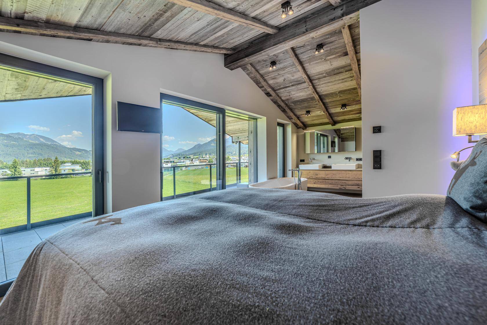 Helles Schlafzimmer mit großem Bett, offenem Badezimmer und Zugang zu einer Terrasse mit Bergblick.