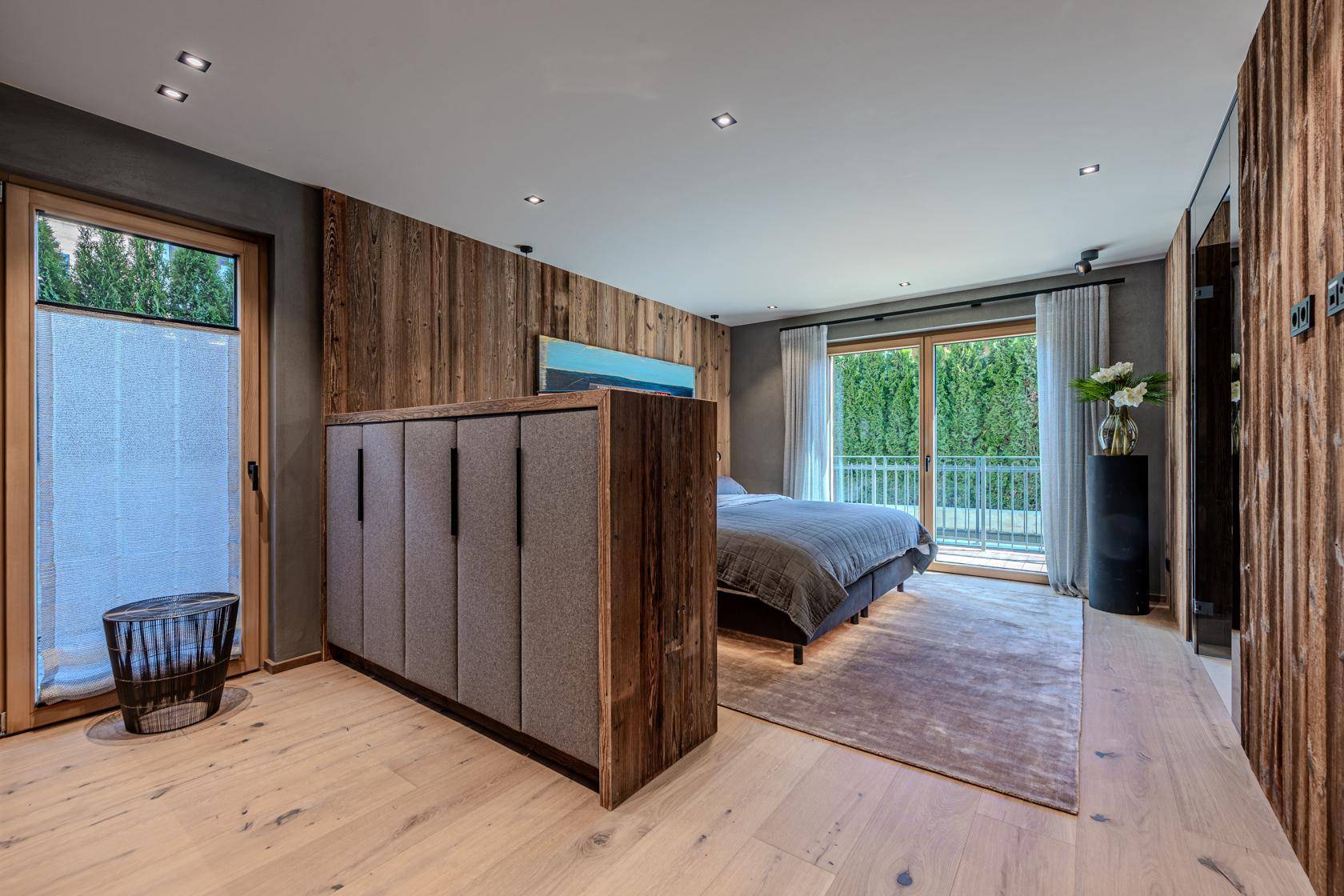 Helles Schlafzimmer mit Holzwänden, großem Bett und Zugang zu einem französischen Balkon.