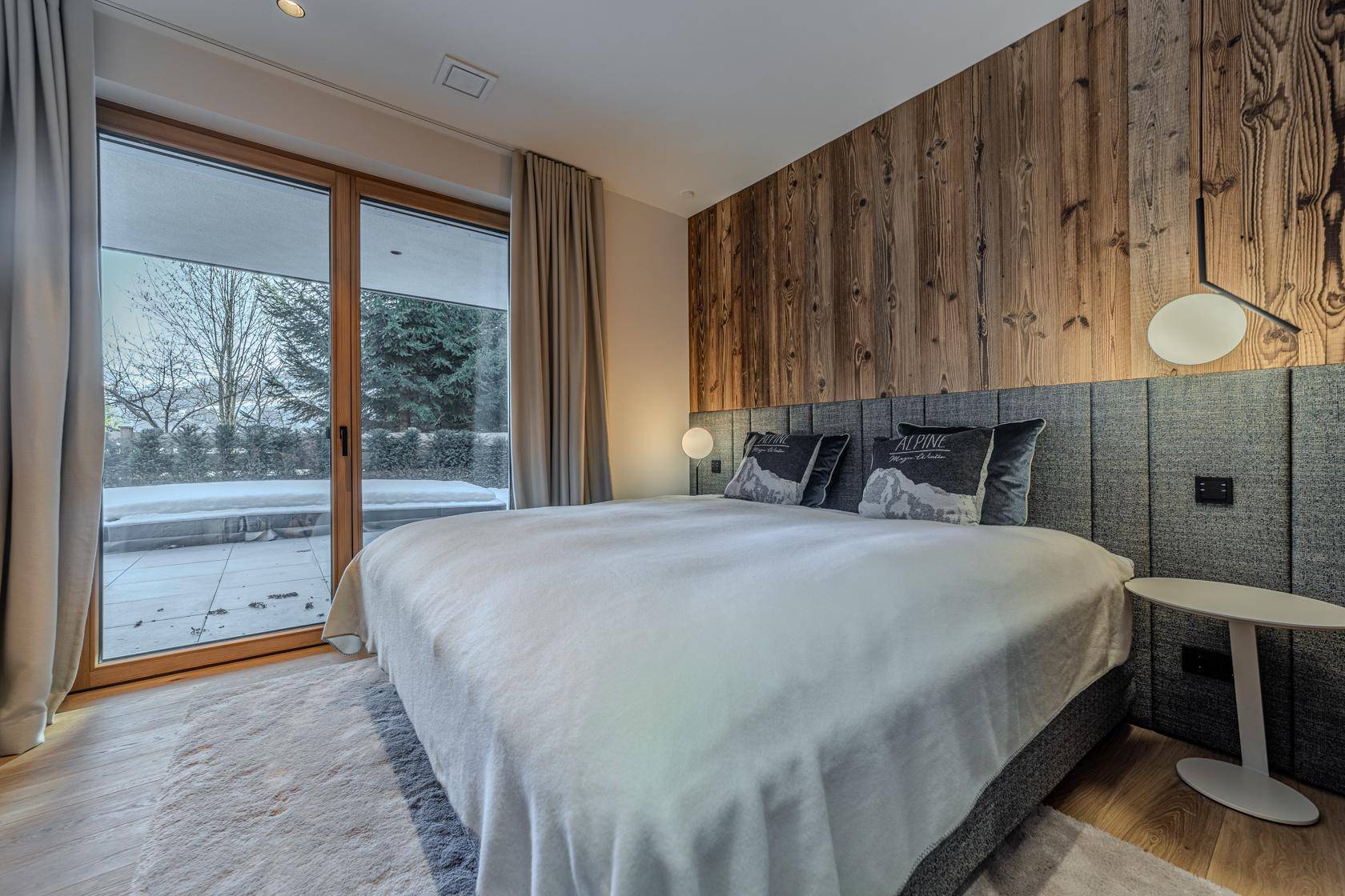 Helles Schlafzimmer mit Holzwand, großem Bett und direktem Zugang zur Terrasse.