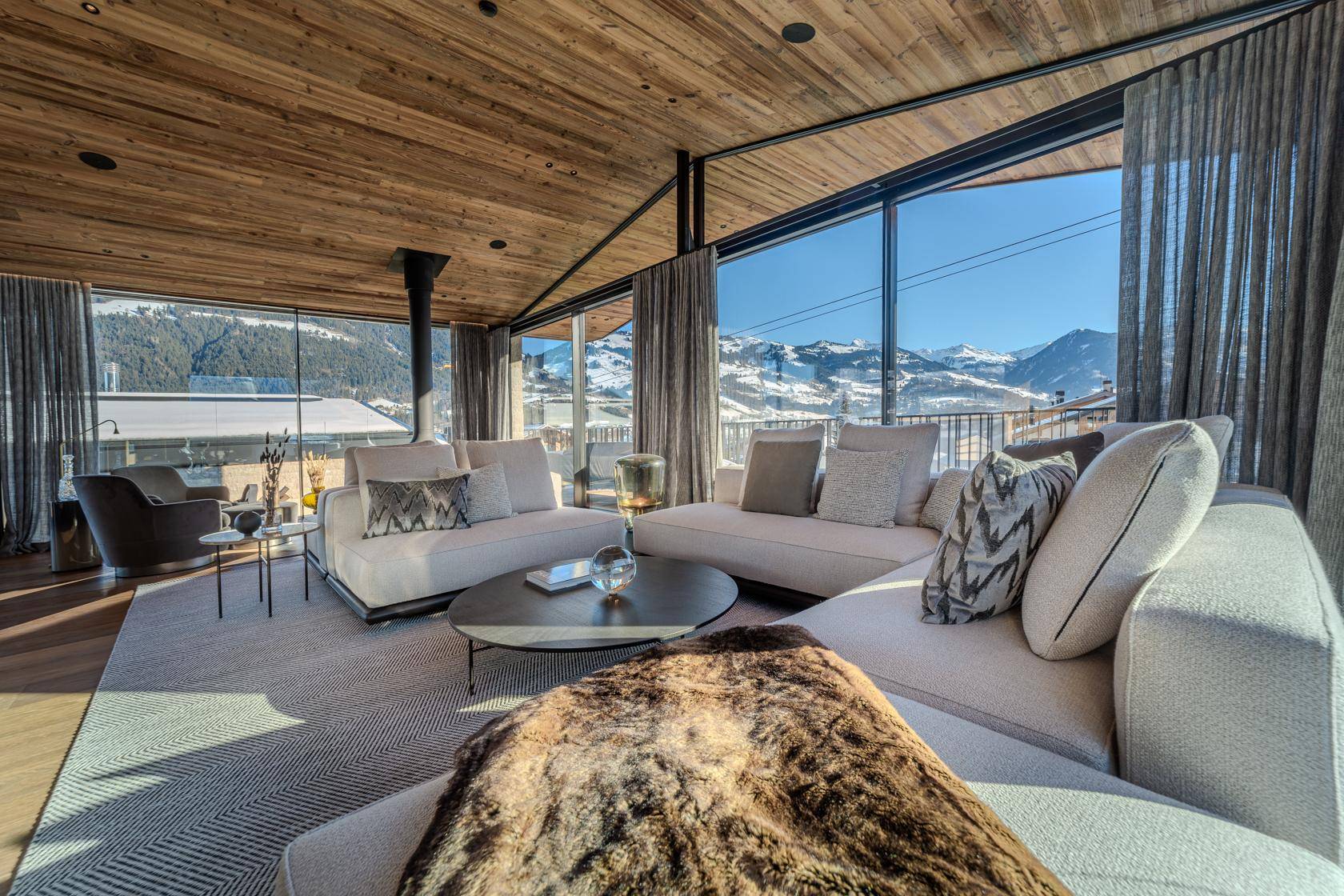 Gemütliches Wohnzimmer mit bequemen Sofas, Teppich und weitem Blick auf die verschneite Berglandschaft.