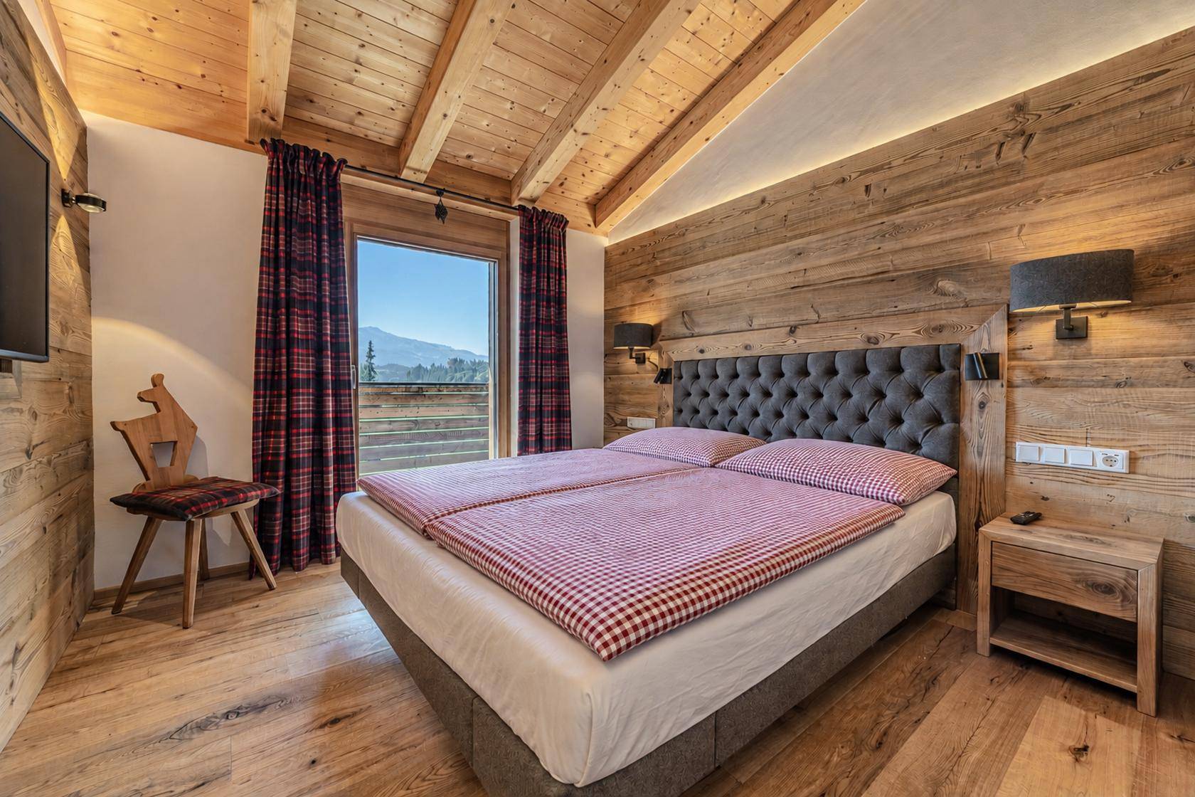Rustikales Schlafzimmer mit Holzwänden, karierter Bettwäsche und Bergblick.
