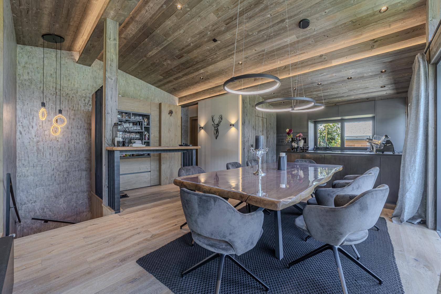 Eleganter Essbereich mit Holztisch, modernen Leuchten und einer stilvollen Bar im Hintergrund.
