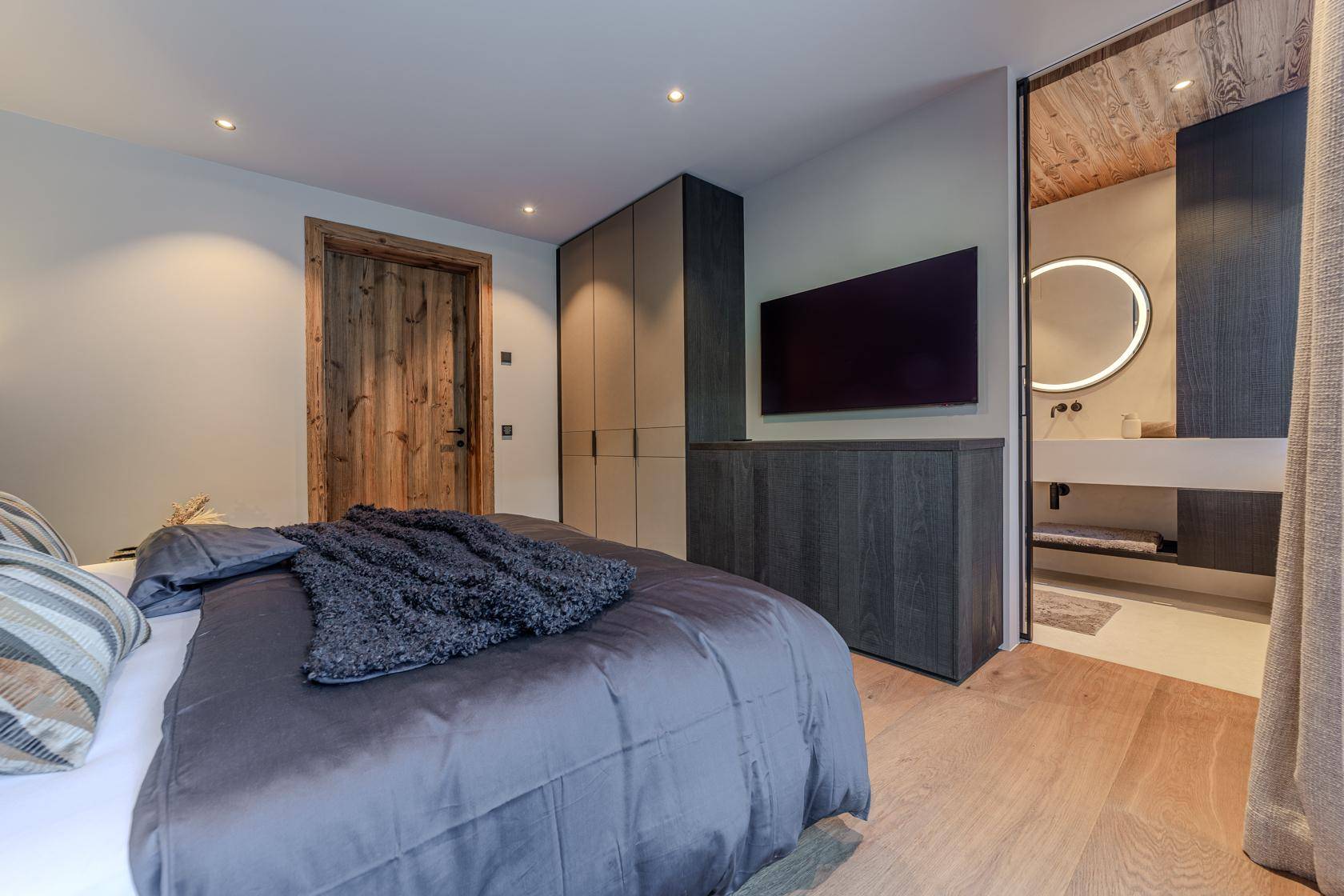 Modernes Schlafzimmer mit Holzboden, Einbauschränken und direktem Zugang zu einem stilvollen Badezimmer.