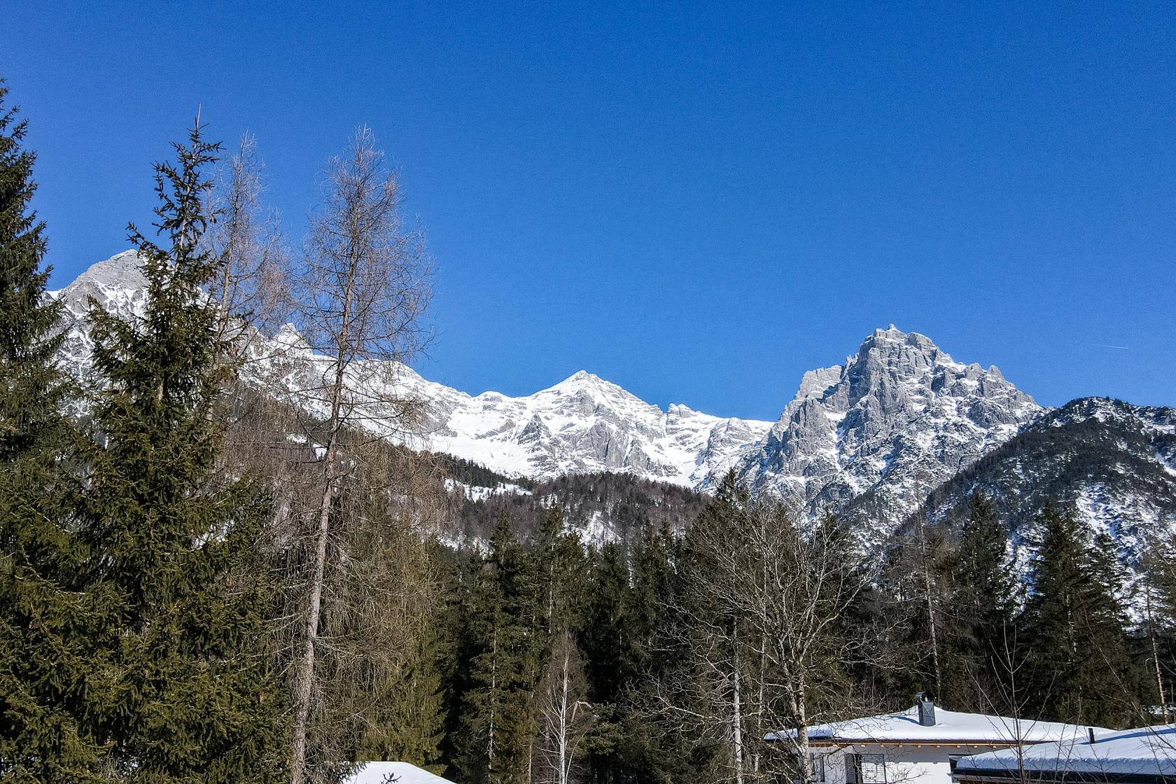 Atemberaubender Blick auf schneebedeckte Berge und Wälder, mit einem Teil des Hauses im Vordergrund.