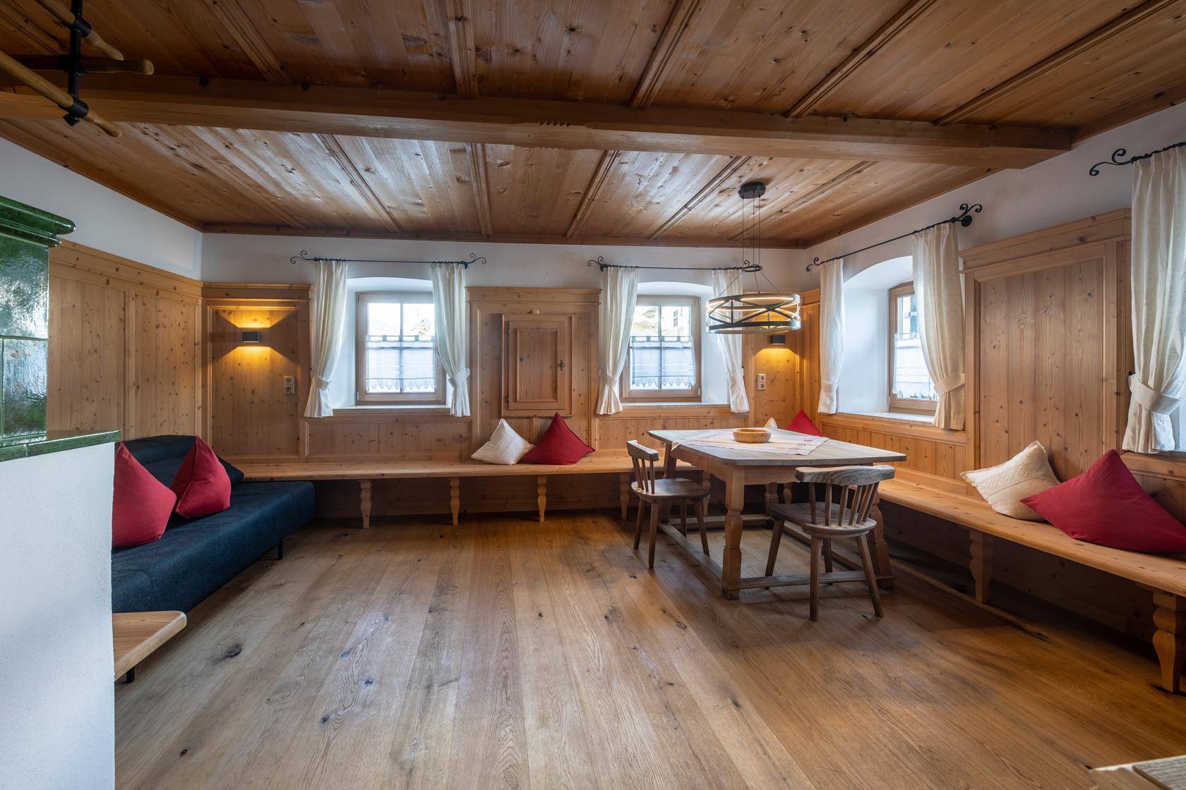 Helles Wohnzimmer mit Holzboden, Kachelofen und traditionellen Holzmöbeln, ideal zum Entspannen.