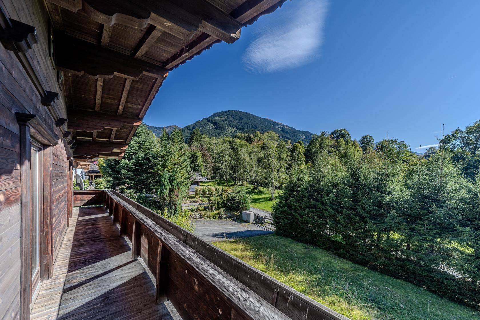 Langer Holzbalkon mit Blick auf grüne Bäume und eine bewaldete Berglandschaft.