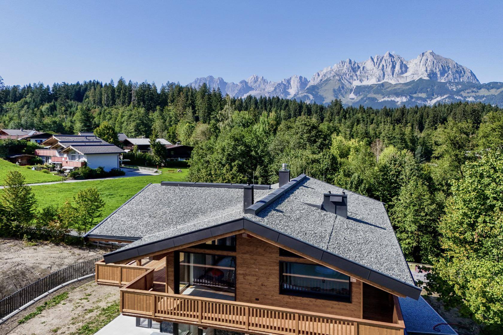 Dachansicht eines modernen Chalets mit Balkonen und Bergblick in grüner Umgebung.