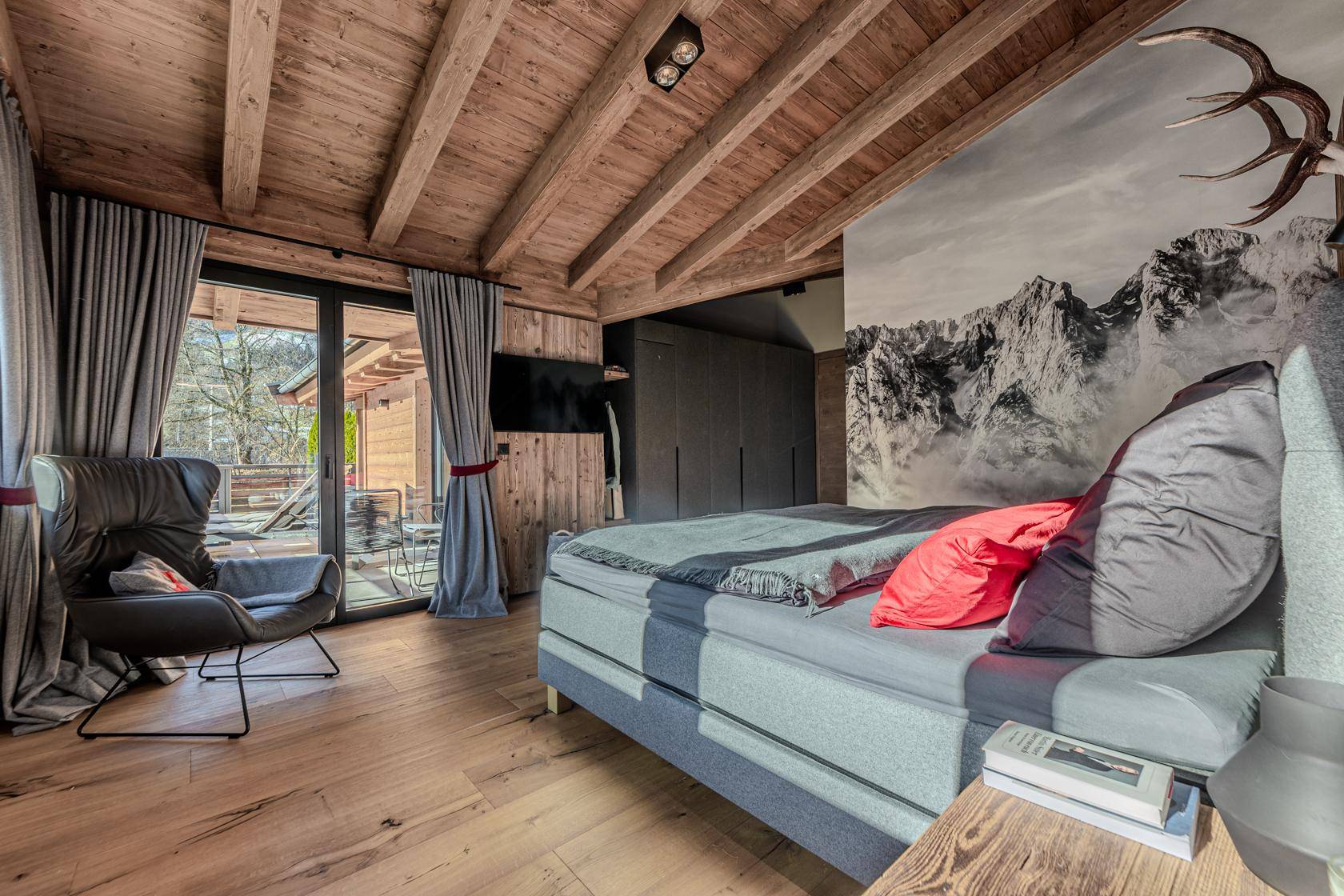Schlafzimmer im Chalet-Stil mit Holzwand, Bergbild-Wandtapete und Zugang zu einem Balkon.