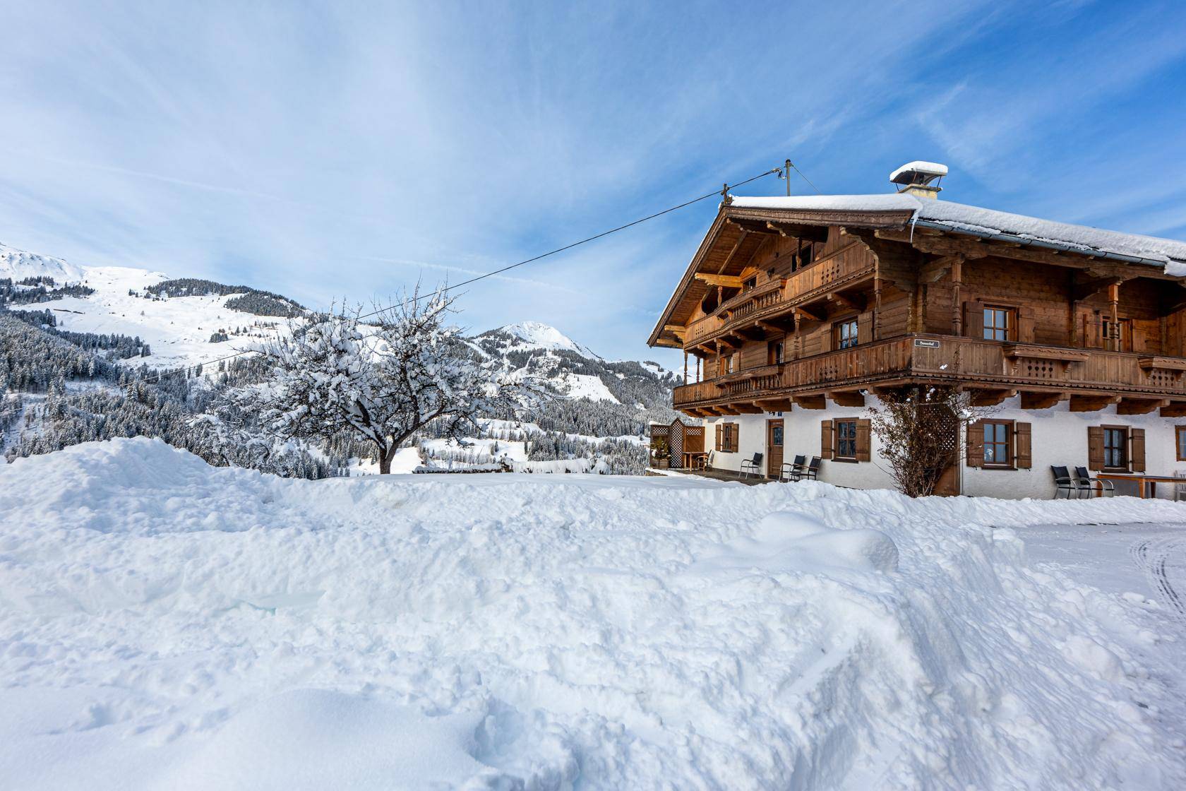 Alpines Holzhaus mit verschneitem Dach und Balkonen, eingebettet in eine idyllische Winterlandschaft.