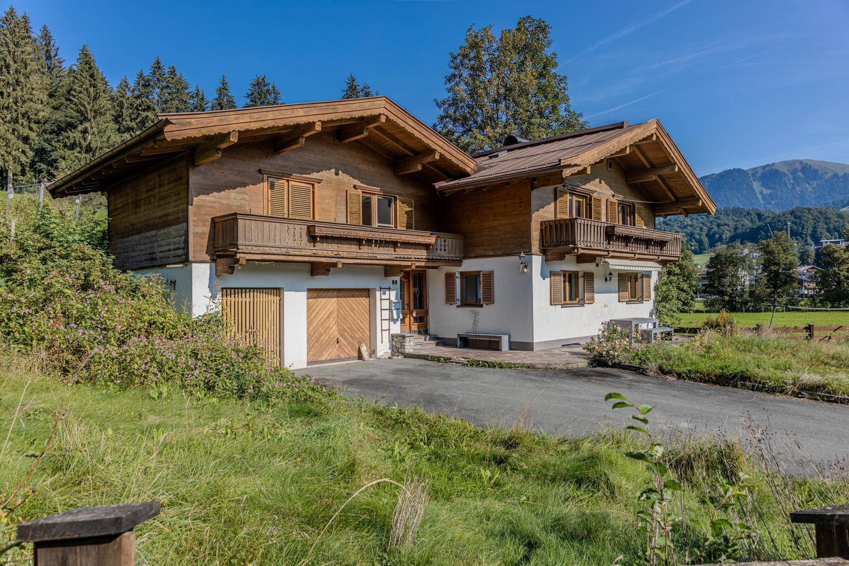 Traditionelles Landhaus mit Holzfassade, Balkonen und Garagenzufahrt in ländlicher Umgebung.