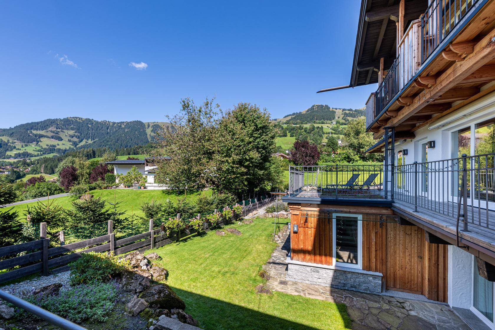 Seitlicher Blick auf das Haus mit gepflegtem Garten, Terrasse und weitem Blick auf die hügelige Landschaft.