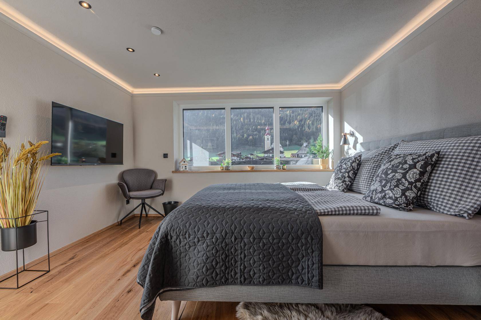 Helles Schlafzimmer mit Holzboden, indirekter Beleuchtung und Blick auf die Umgebung.
