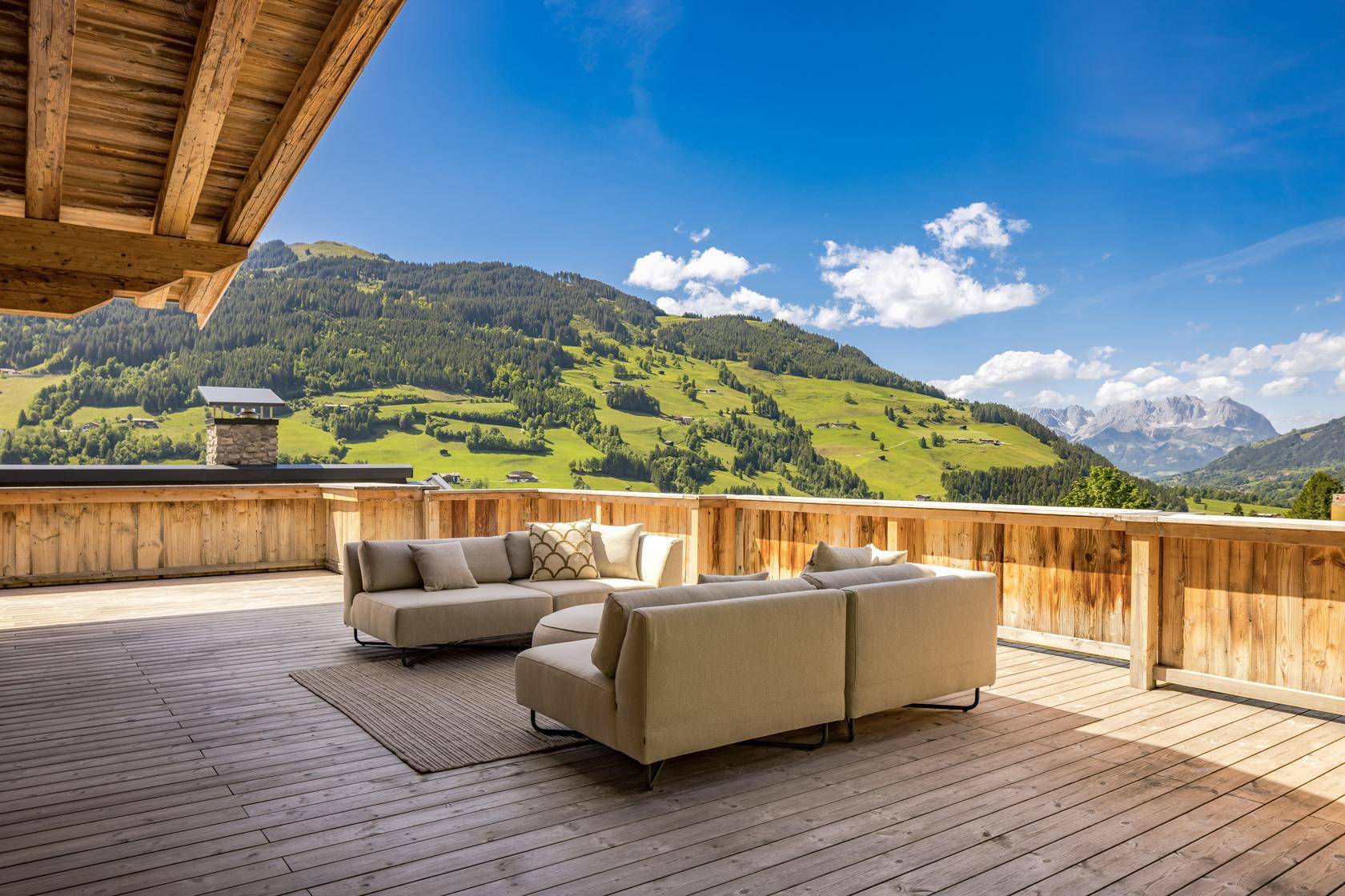 Große Holzterrasse mit bequemen Loungemöbeln und atemberaubendem Bergblick.