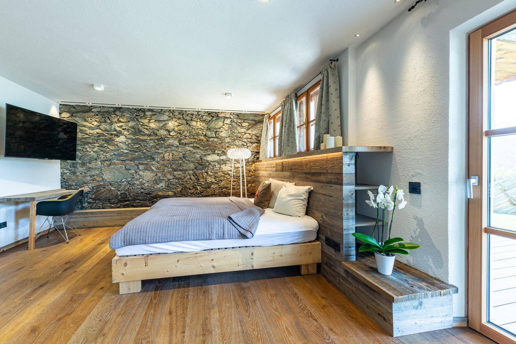 Modernes Schlafzimmer mit Holzboden, Steinwand und Zugang zum Außenbereich.