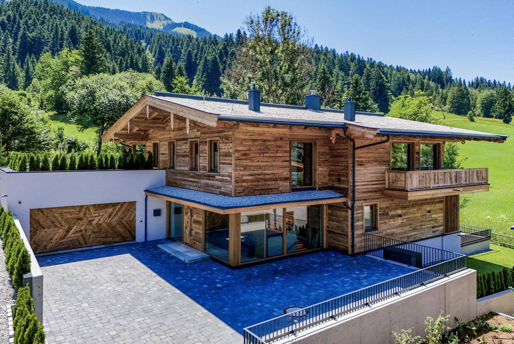 Modernes Chalet mit Holzfassade, großen Fenstern und Doppelgarage in alpiner Umgebung.