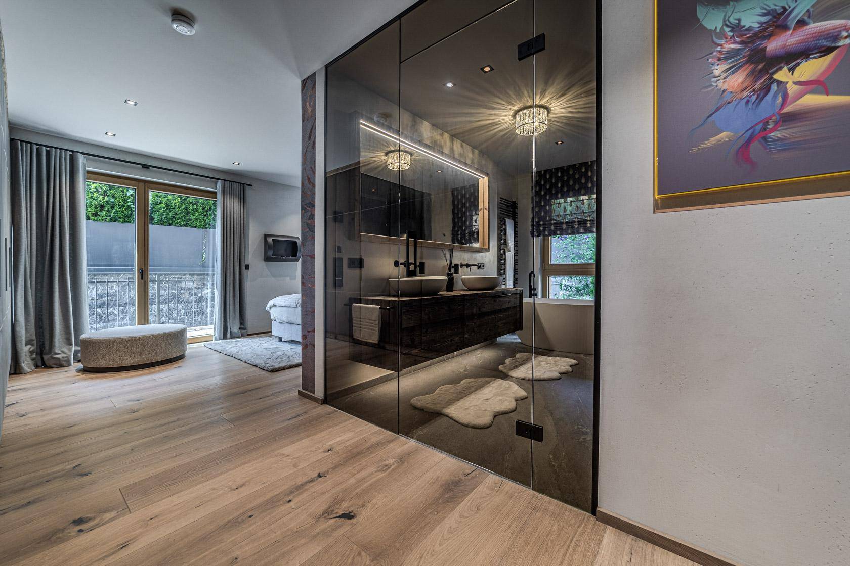Offenes Badezimmer mit Doppelwaschbecken, Glasdusche und Badewanne, vom Schlafzimmer aus sichtbar.
