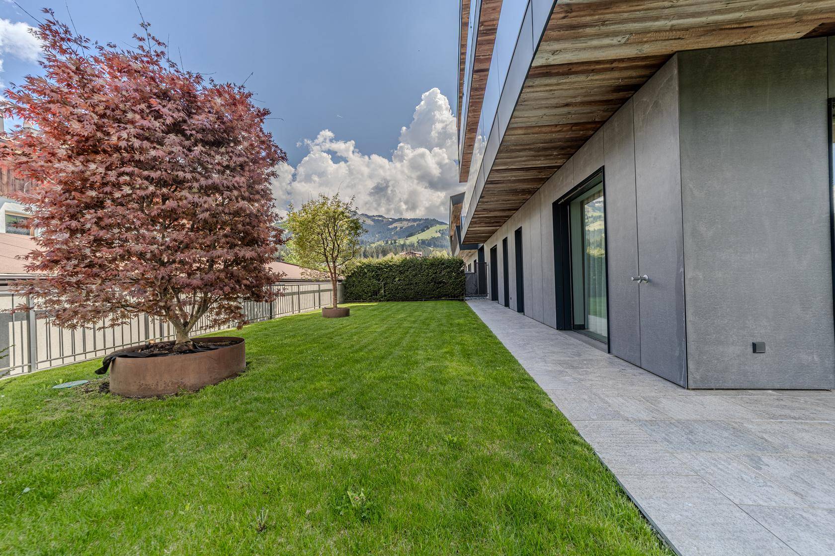 Gepflegter Gartenbereich mit Rasenfläche und Bäumen neben dem modernen Gebäude.