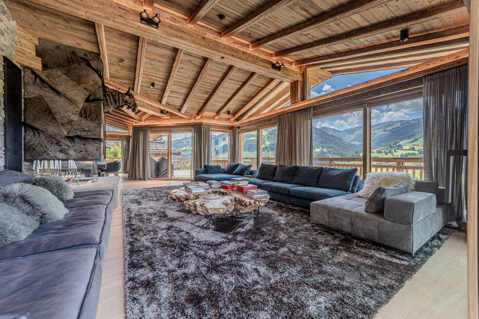 Elegantes Wohnzimmer mit Holzbalkendecke, großzügigen Sofas und beeindruckendem Bergblick durch große Fenster.
