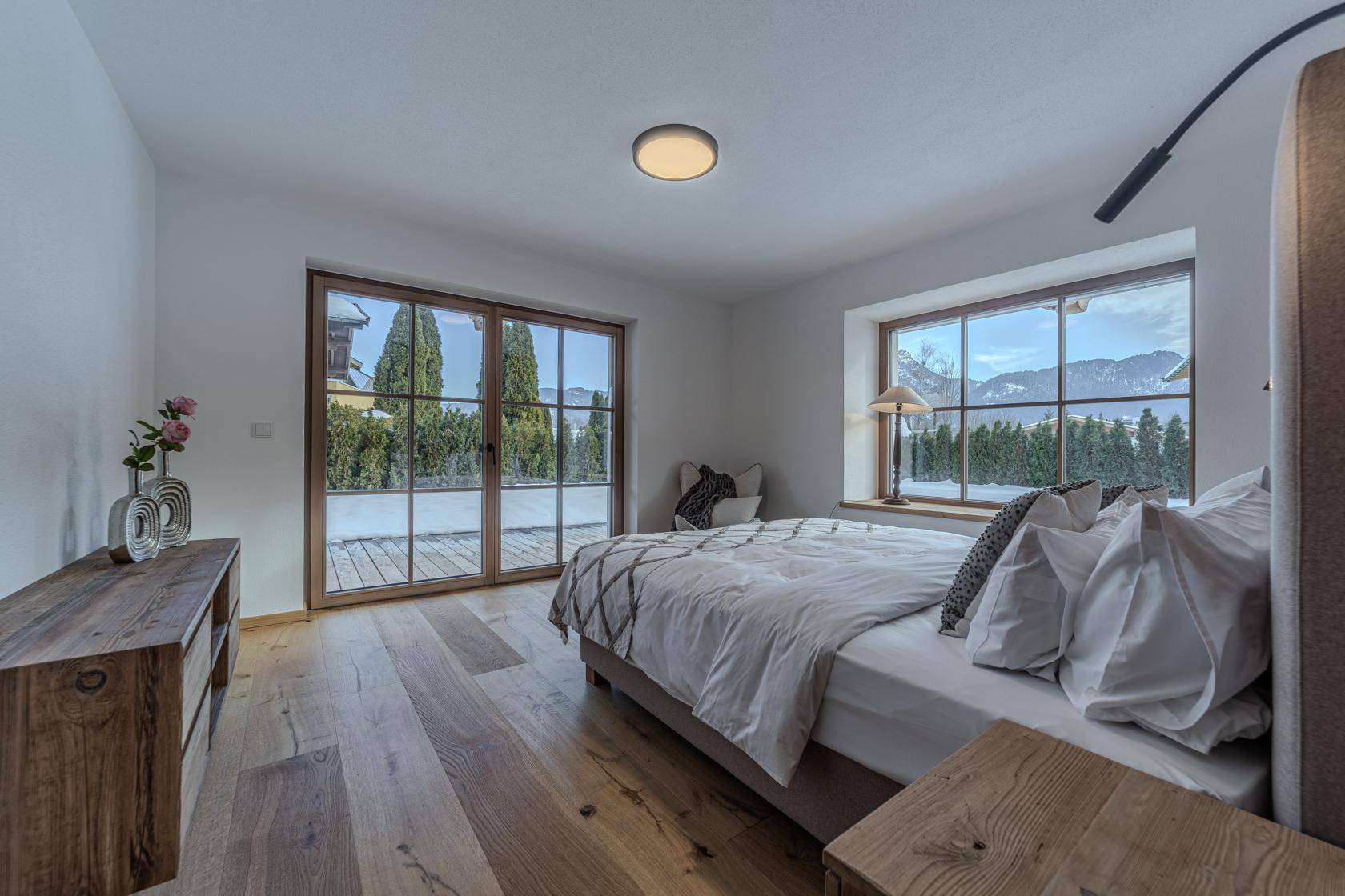 Helles Schlafzimmer mit Holzboden, großen Fenstern und Zugang zum Gartenbereich.