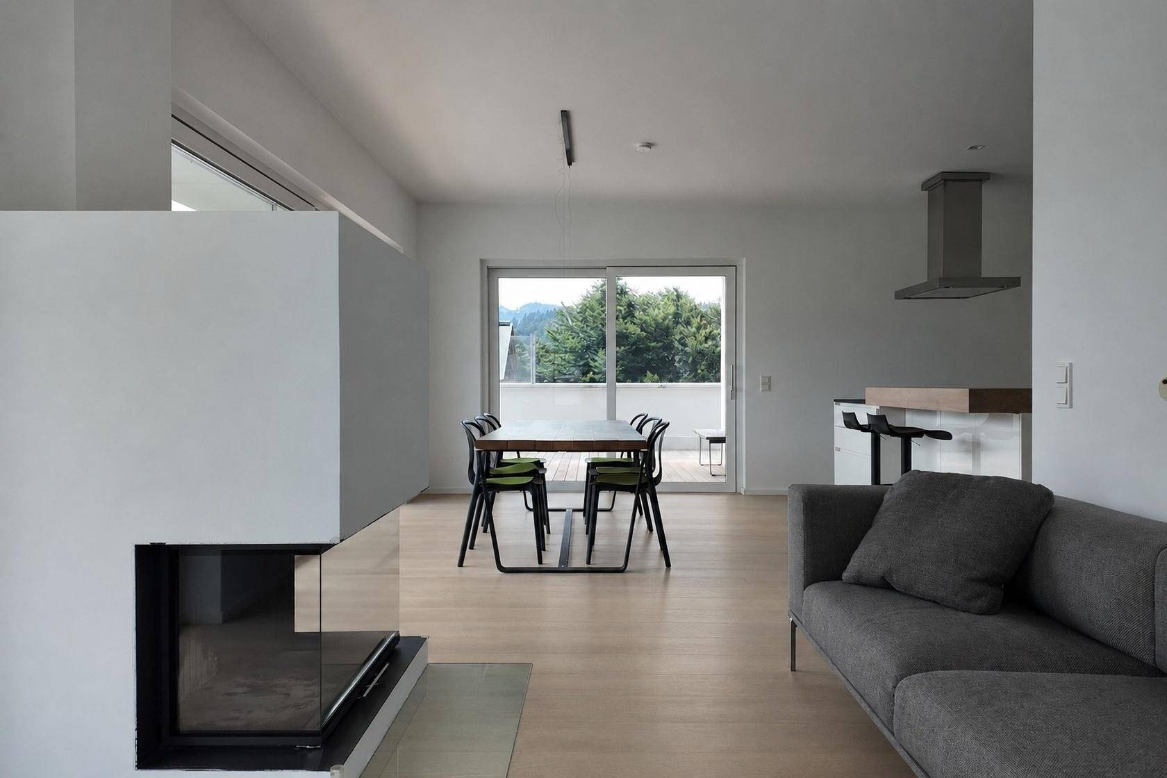 Heller Wohnbereich mit grauem Sofa, modernem Kamin und Zugang zu einem Balkon mit grüner Aussicht.