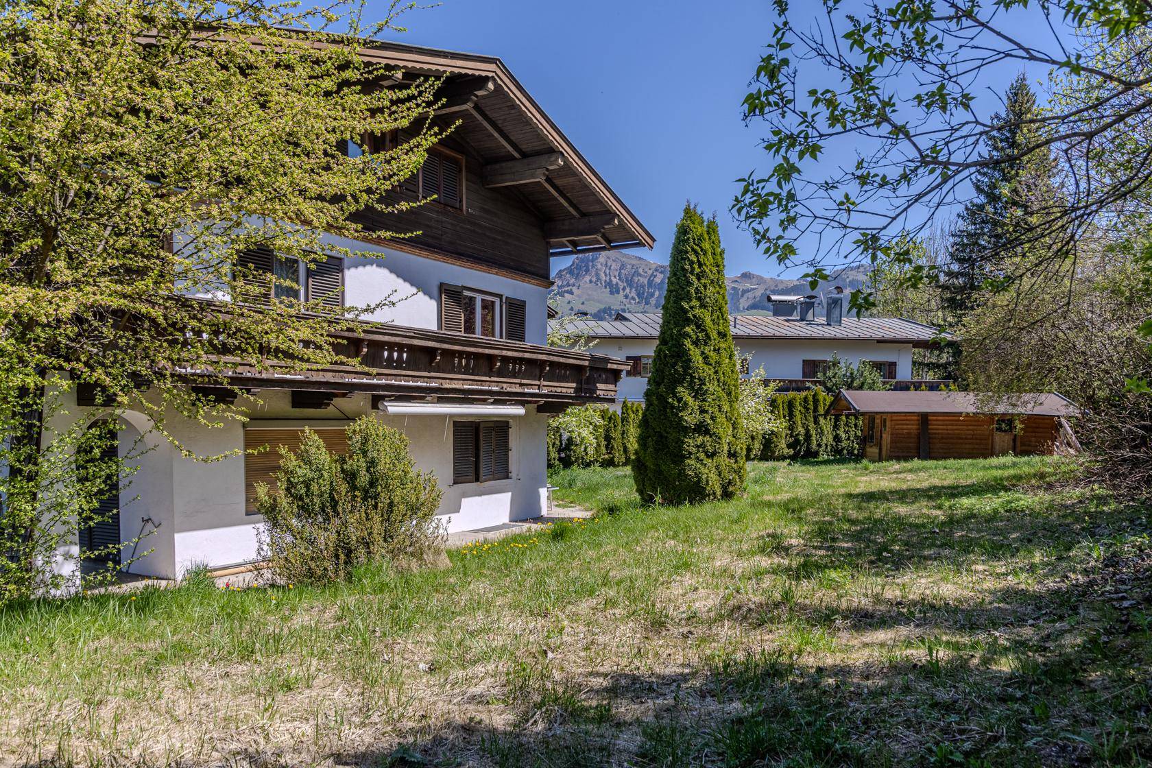Hausfassade mit traditionellem Holzbalkon, umgeben von einem gepflegten Garten und Bergblick.