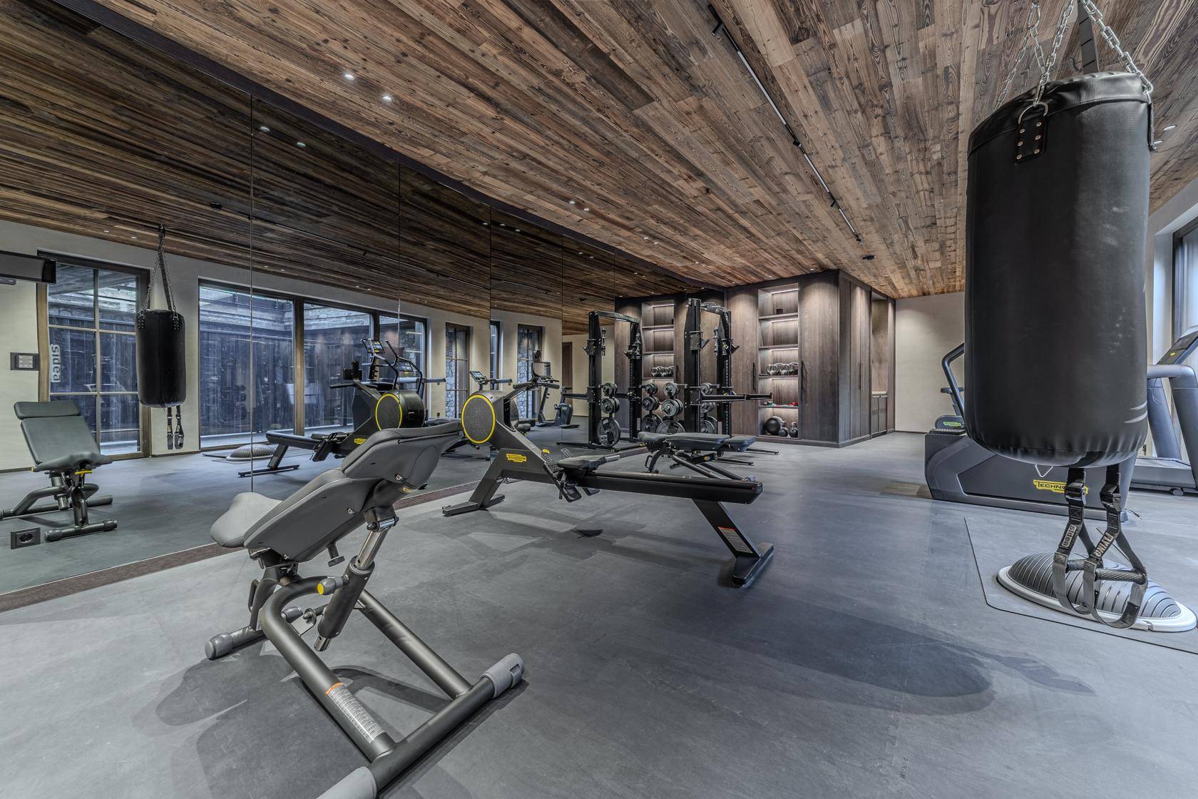 Moderner Fitnessraum mit hochwertigen Geräten, Holzbalkendecke und großen Spiegelflächen.