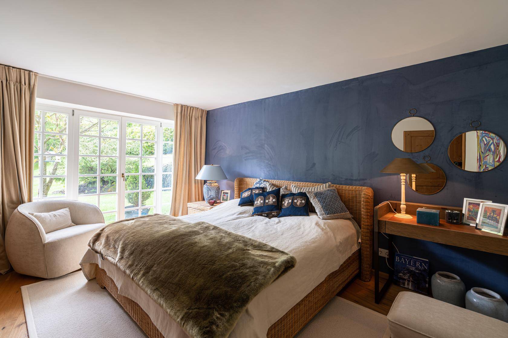 Helles Schlafzimmer mit Doppelbett, blauer Akzentwand und Zugang zum Garten.