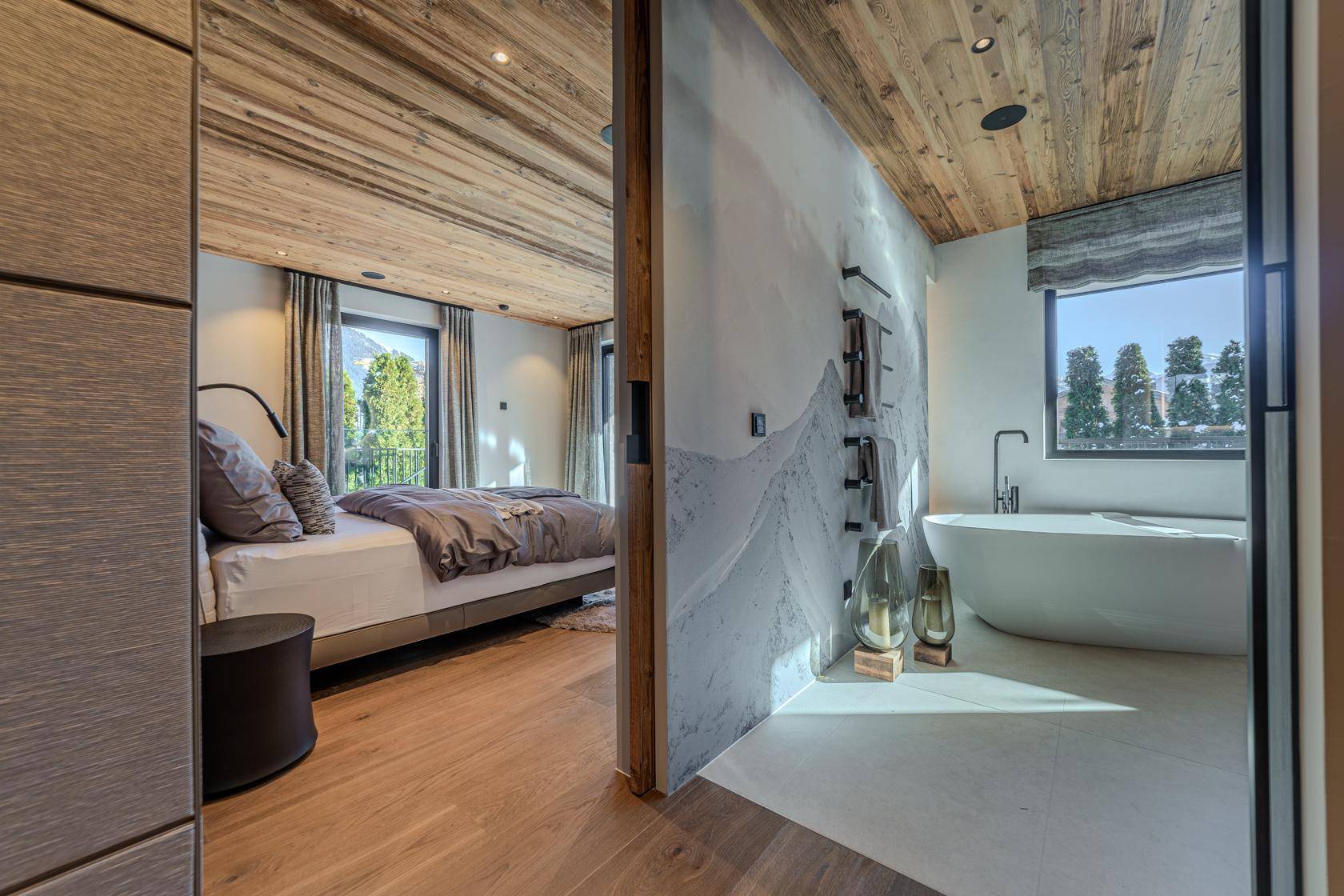 Modernes Schlafzimmer mit Holzbalkendecke und angrenzendem Badezimmer mit freistehender Badewanne.
