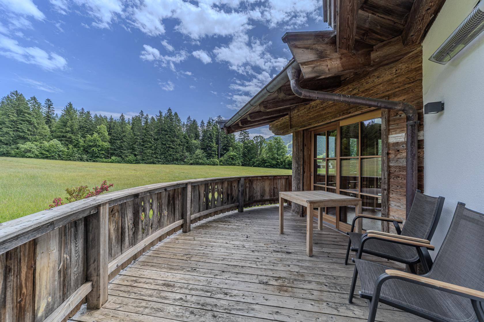 Langer Holzbalkon mit Blick auf weite Wiesen und Wälder unter blauem Himmel.