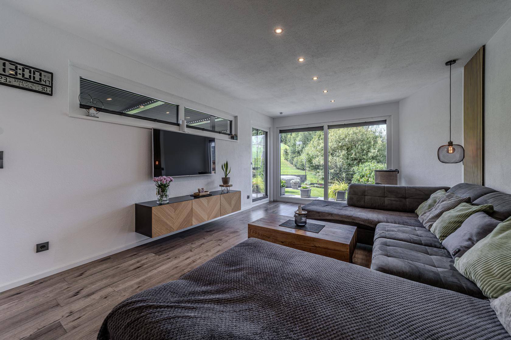 Modernes Wohnzimmer mit großem Sofa, Fernseher und Zugang zum Garten mit Bergblick.