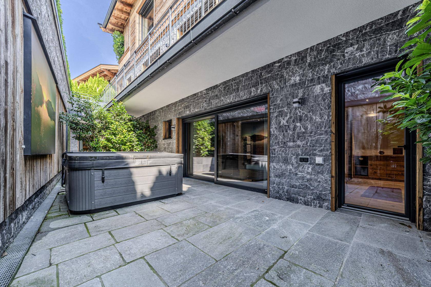 Private Terrasse mit Whirlpool und direktem Zugang zur Sauna, umgeben von Grün.