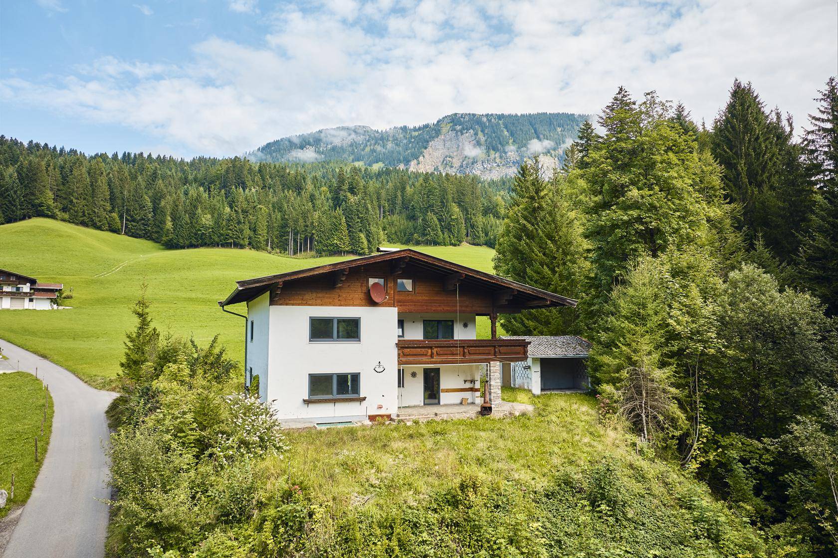 Traditionelles Haus mit Holzbalkon und weißer Fassade, umgeben von grüner Natur.