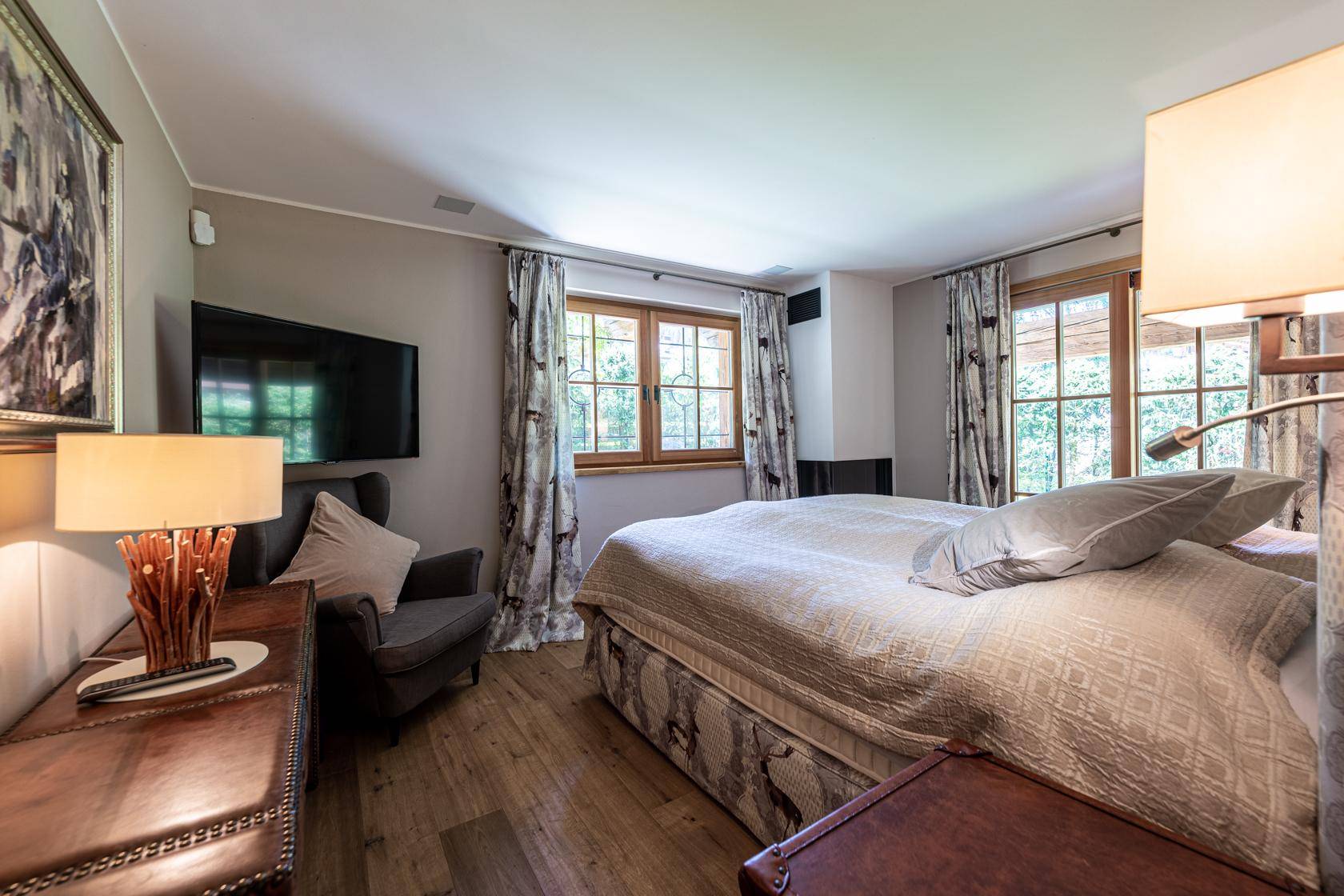 Helles Schlafzimmer mit großem Bett, Fernseher und zwei Fenstern mit Blick ins Grüne.